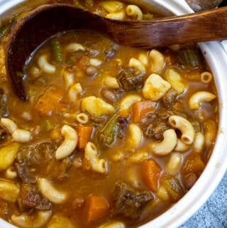 Close up of a bowl of beef minestrone soup with a wooden serving spoon.
