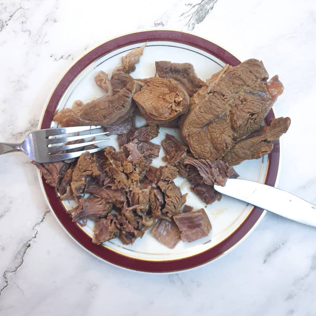 Shin beef being shredde on a plate.