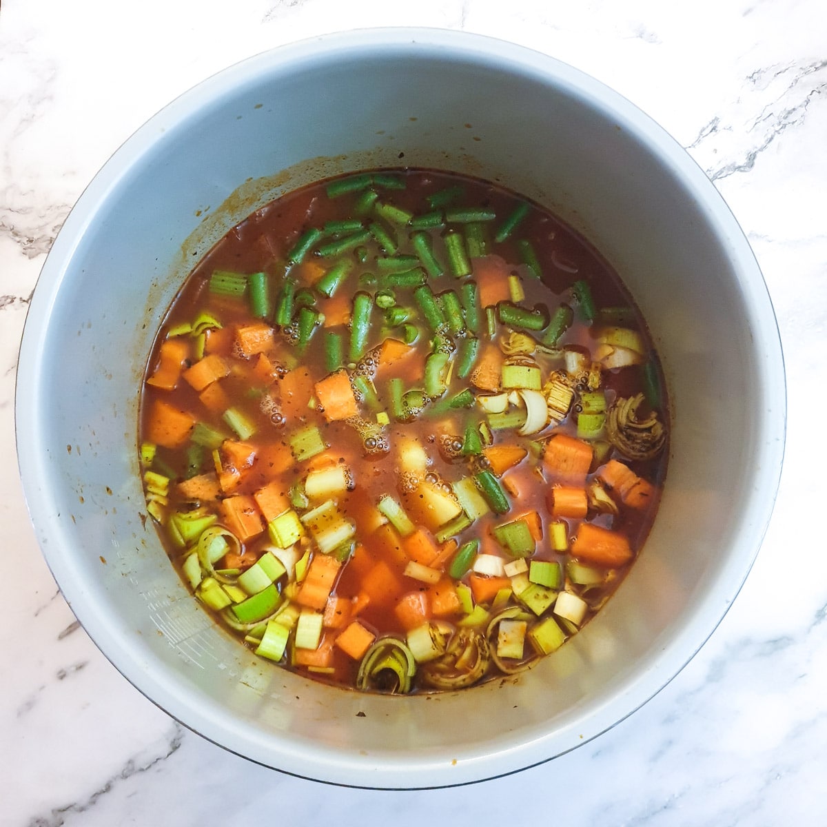 Diced vegetables added to the soup in a pressure cooker.