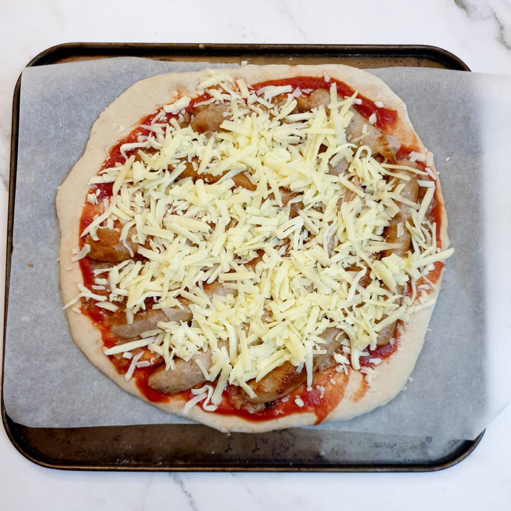 Ingredients for a sausage and caramelised onion pizza on the pizza dough.