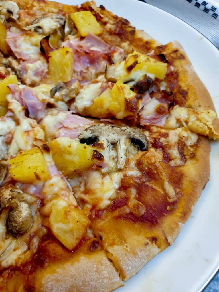 Overhead shot of a Hawaiian pizza covered with ham, mushrooms and tomatoes.