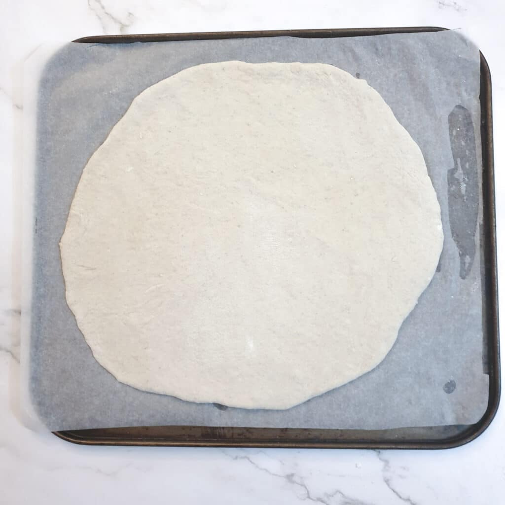 Pizza dough rolled into a 12" circle on a baking tray.