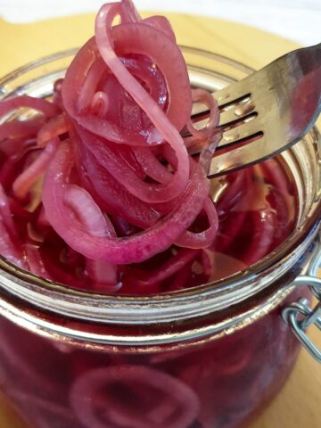 A forkful of pickled red onions being lifted from a jar.