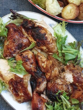 Cooked spatchcock chicken pieces on a serving plate next to a dish of vegetables.