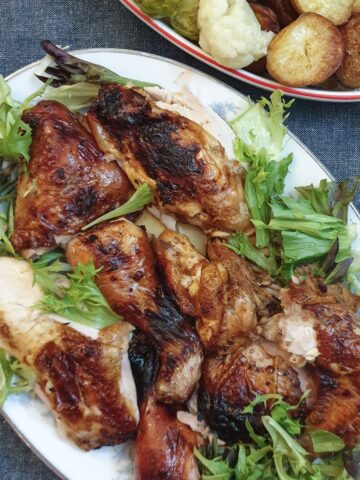 Cooked spatchcock chicken pieces on a serving plate next to a dish of vegetables.