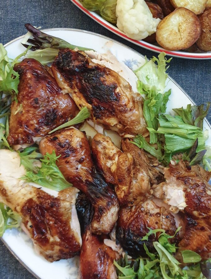 Cooked spatchcock chicken pieces on a serving plate next to a dish of vegetables.