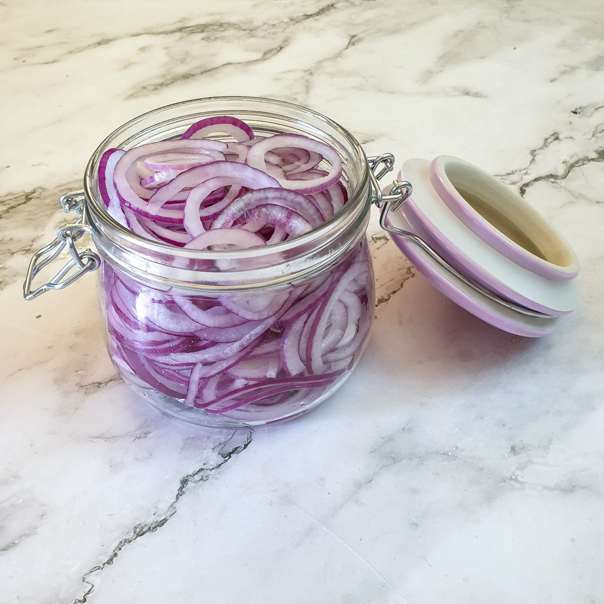 Slices of red onions packed into a glass jar.
