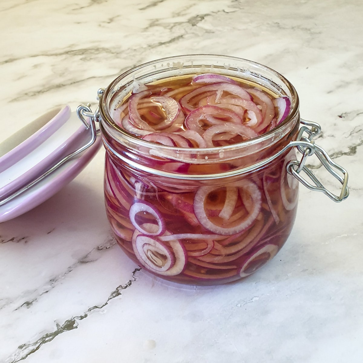 Slices of red onion in a glass jar, covered with pickling liquid.