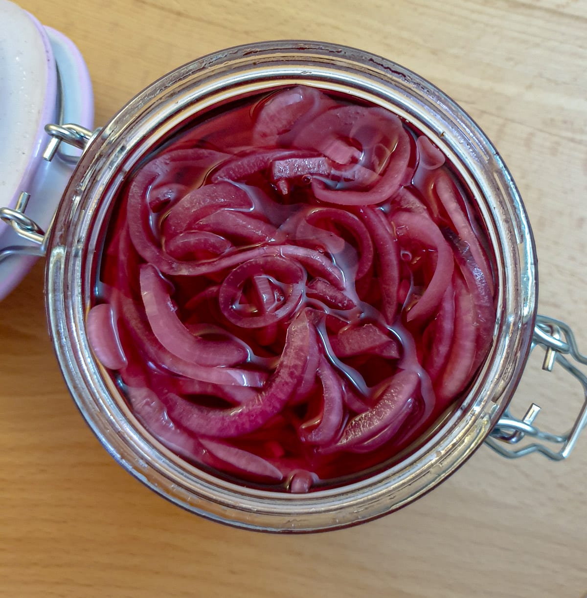 Overhead closeup of pickled red onions in a glass jar.