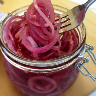 A forkful of pickled red onions being lifted from a jar.
