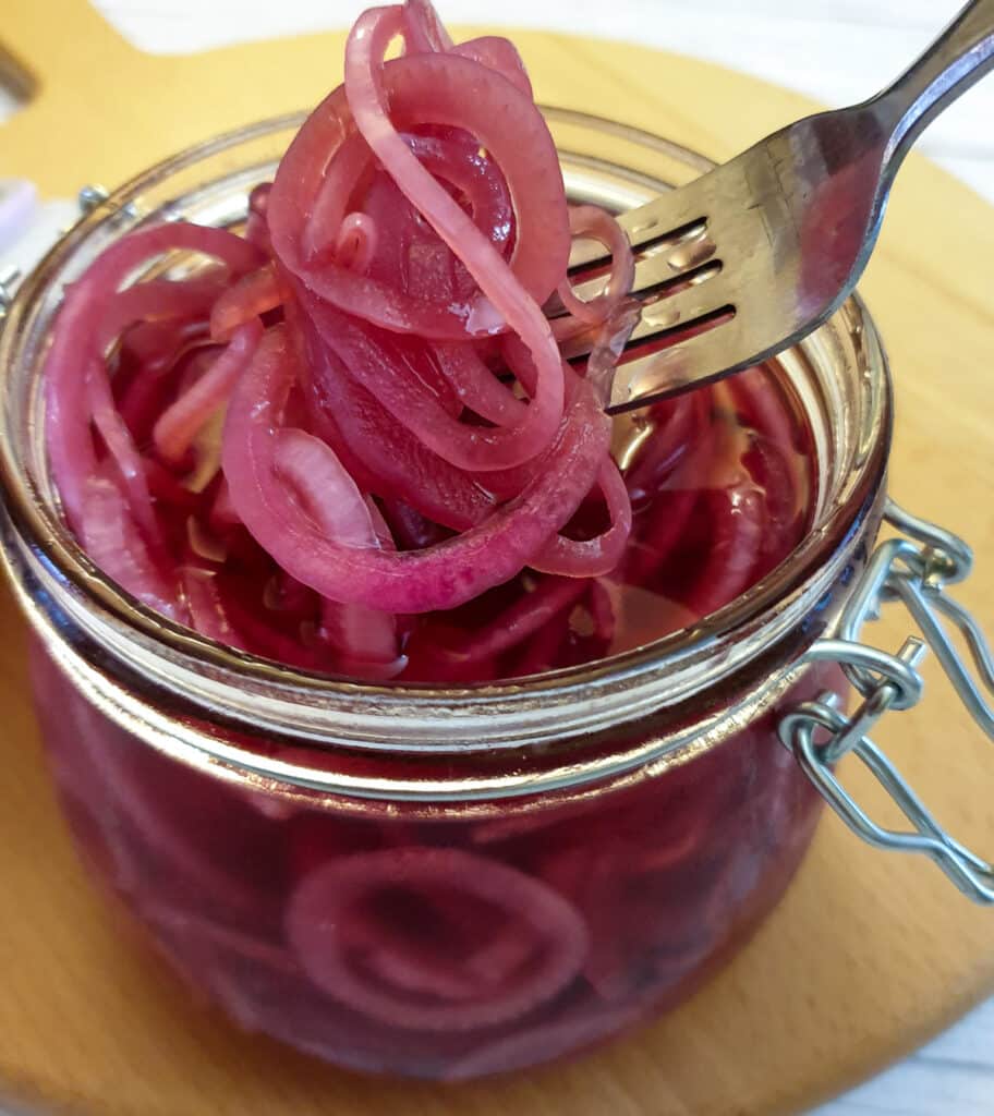 A forkful of pickled red onions being lifted from a jar. A forkful of pickled red onions being lifted from a jar.