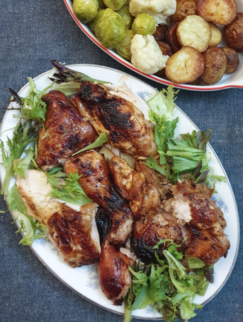 Cooked spatchcock chicken pieces on a serving plate next to a dish of vegetables.