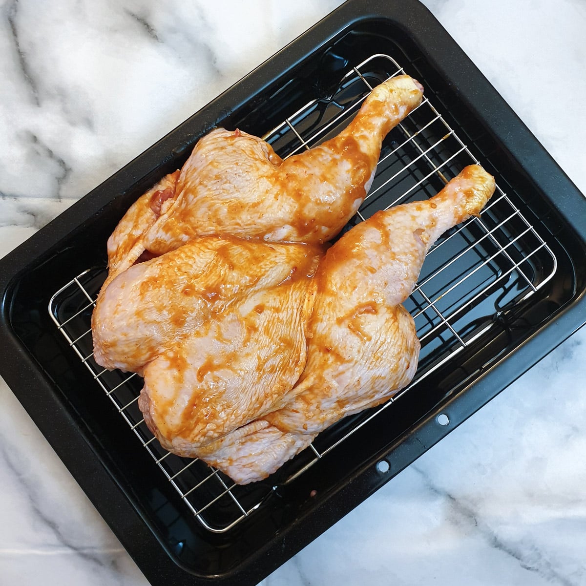 A spatchcock chicken covered in peri peri marinade, in a roasting pan.