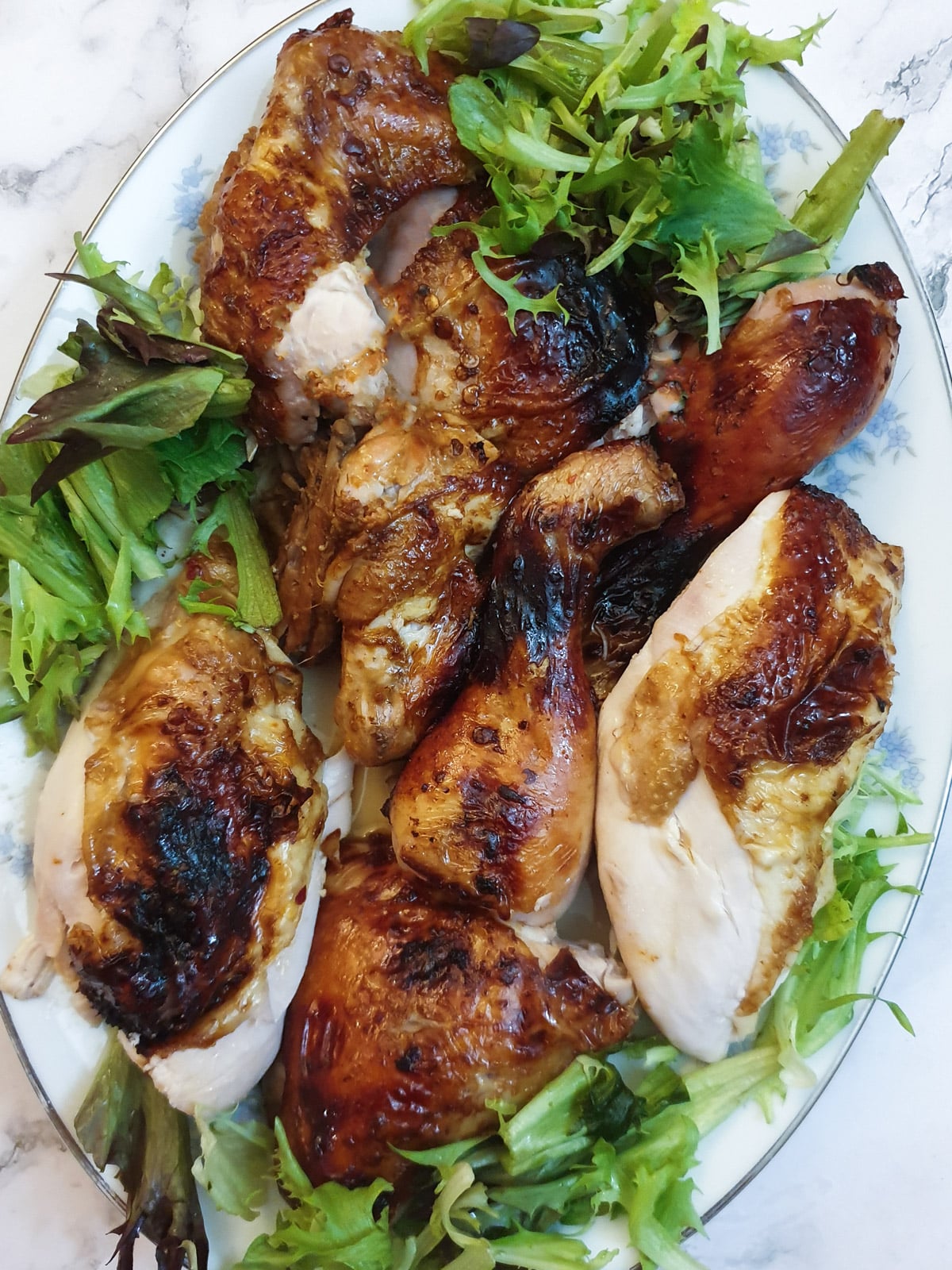 A plate of carved pieces of cooked spatchcocked chicken on a bed of lettuce.