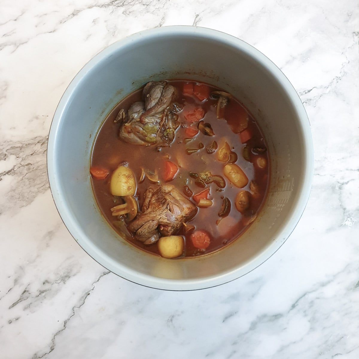 Cooked lamb shanks and vegetables in gravy in a pressure cooker.