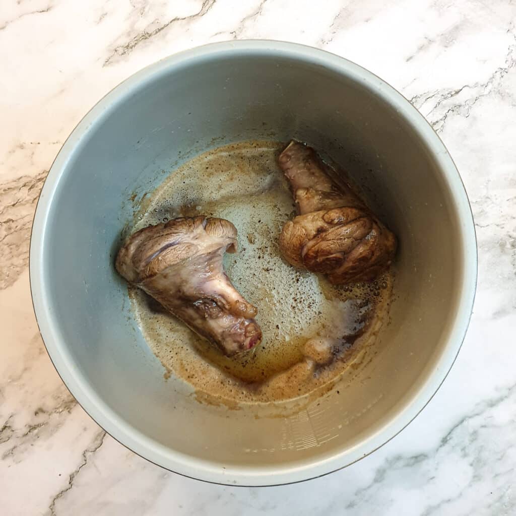 2 lamb shanks browning in butter in the inner pot of a pressure cooker.