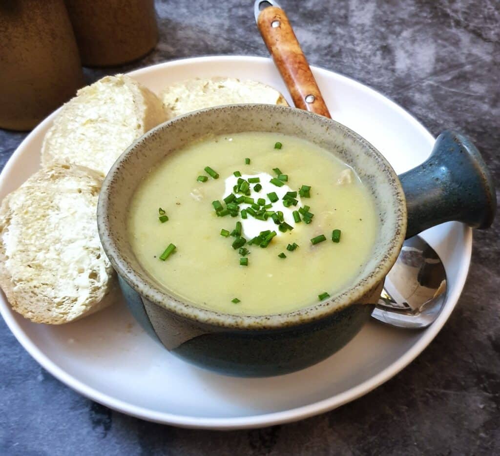 A bowl of potato and leek soup in a soup dish, garnished with creme fraiche and chopped chives.