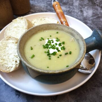 A bowl of potato and leek soup in a soup dish, garnished with creme fraiche and chopped chives.