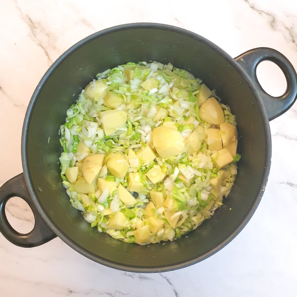 Softened potatoes, leeks and onions in a saucepan.