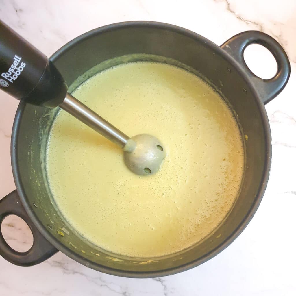 Potato and leek soup being blended with a stick blender in a saucepan.