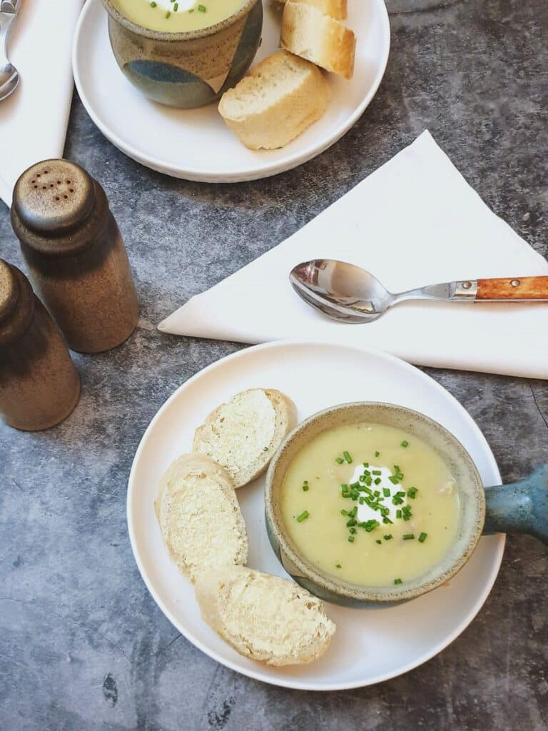 Overhead shot of potato and leek soup in a soup bowl with slices of crusty bread.