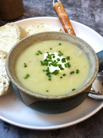 A bowl of potato and leek soup in a soup dish, garnished with creme fraiche and chopped chives.