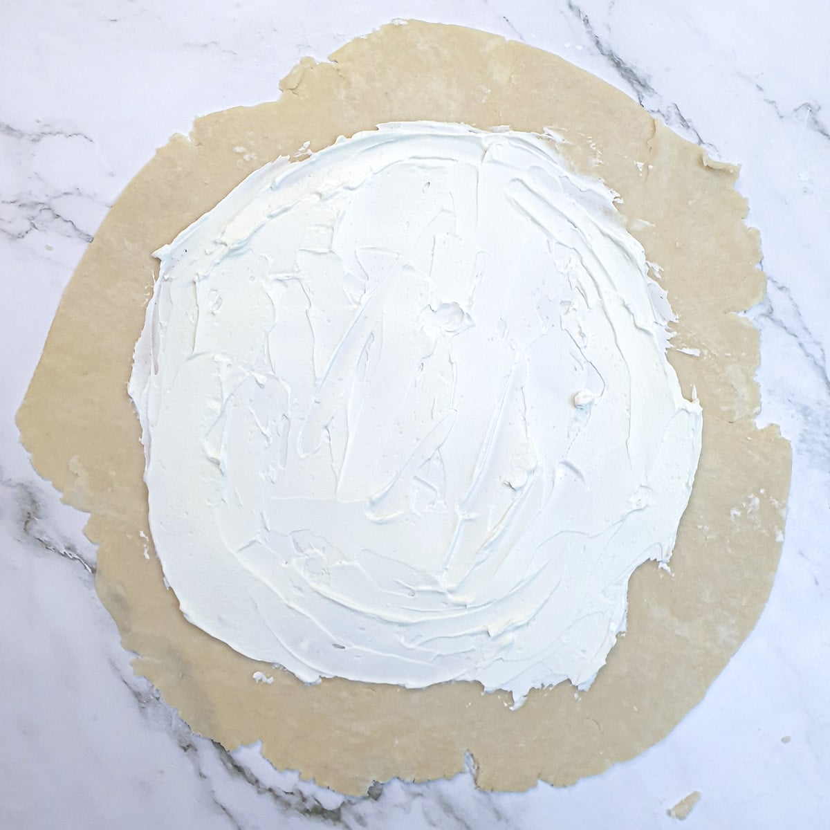 Dough rolled into a circle and spread with cream cheese.