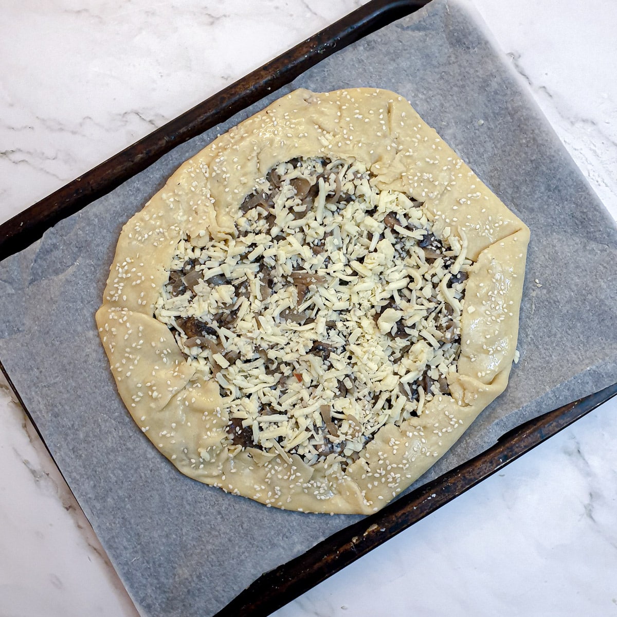 An unbaked mushroom galette on a baking tray.