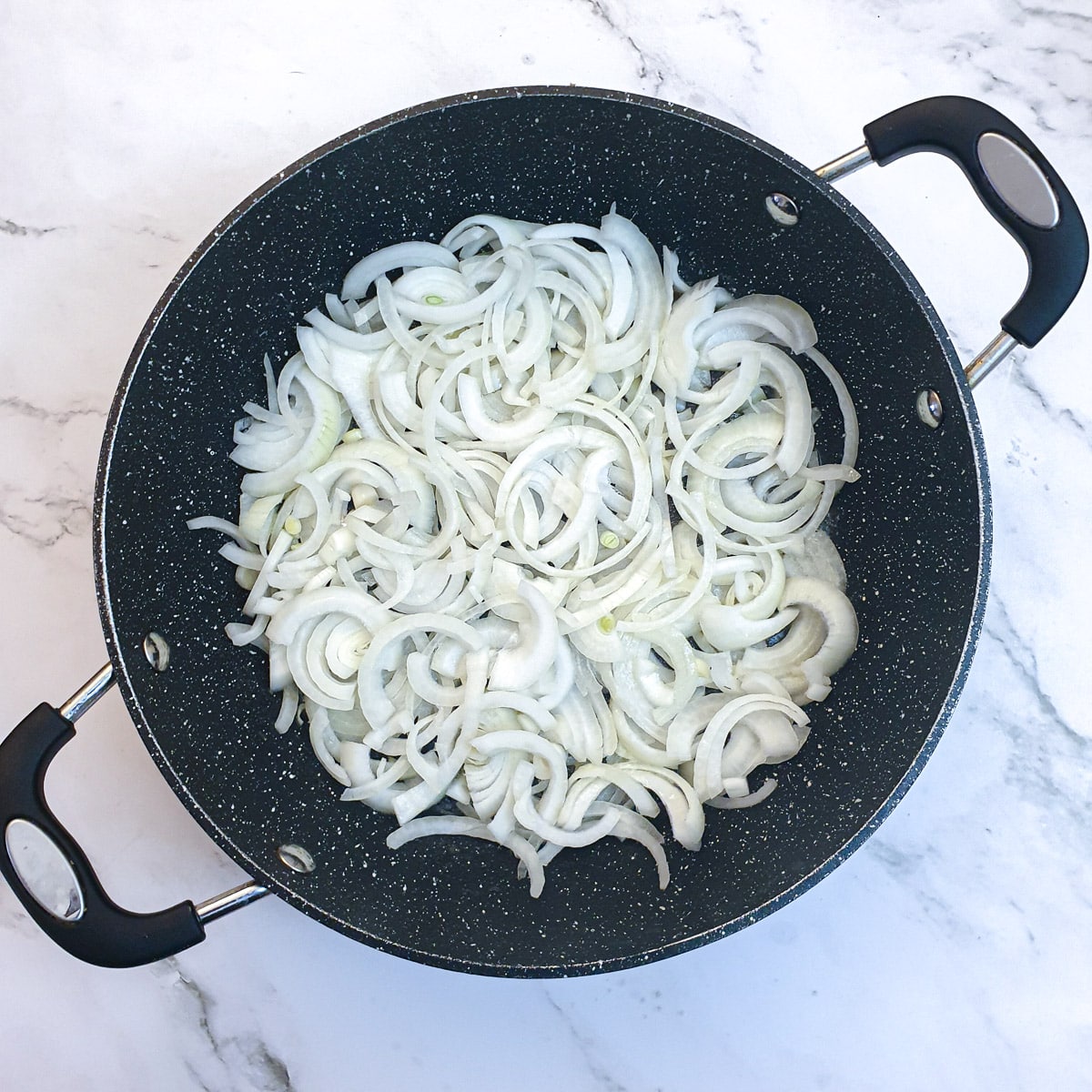 Sliced onions in a frying pan being sauteed in butter.