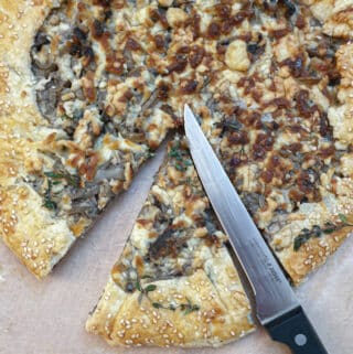 Overhead shot of a mushroom galette being cut into slices with a knife.