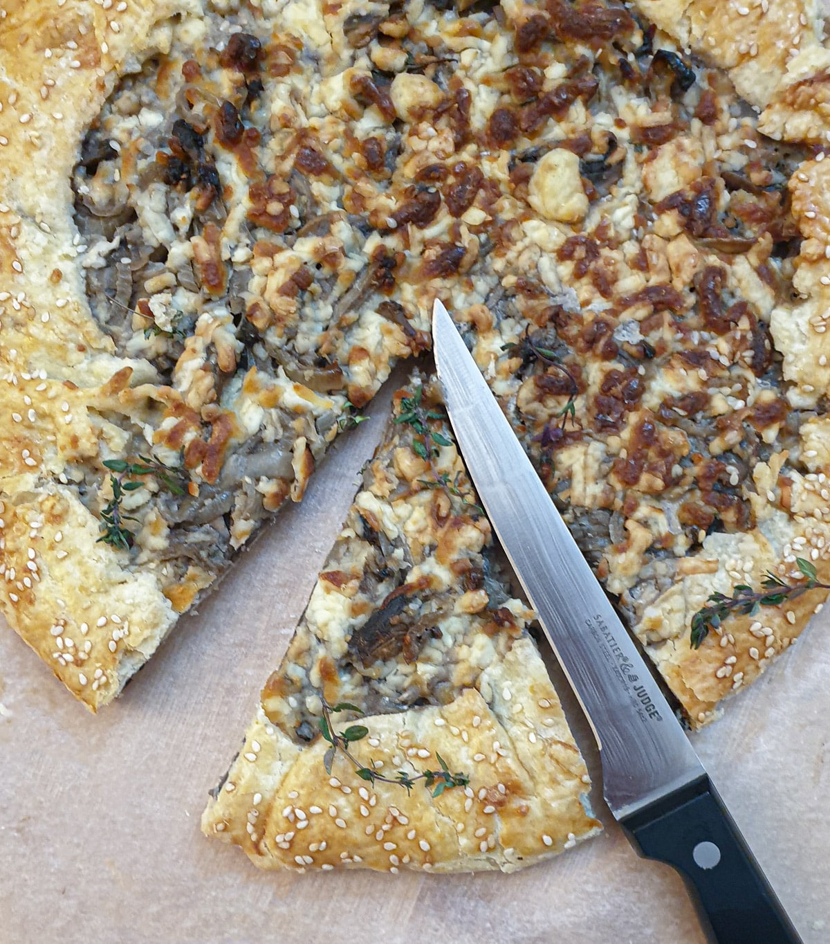 Overhead shot of a mushroom galette being cut into slices with a knife.