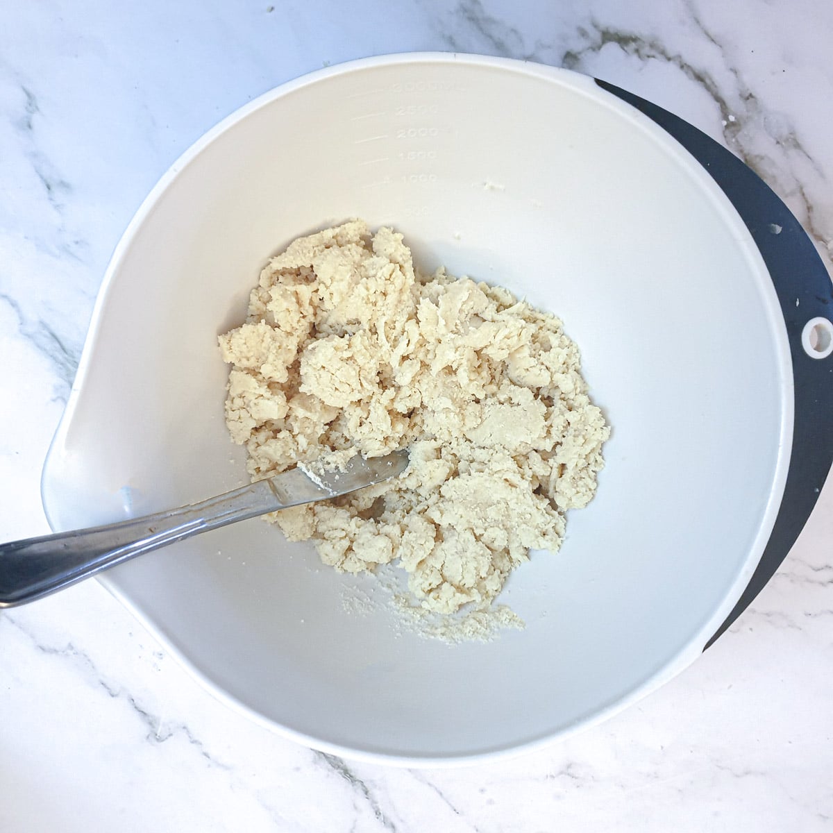 Dough being mixed in a bowl with a flat knifie until it starts to come together.