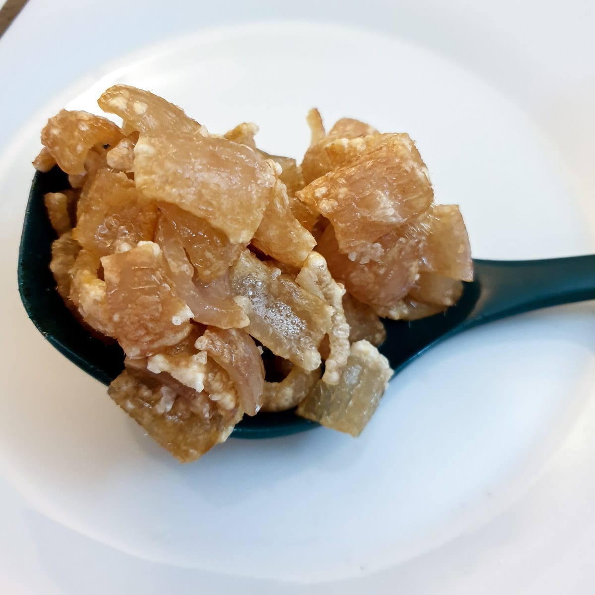 Par-cooked pork scratchings on a spoon showing the skin starting to crisp.