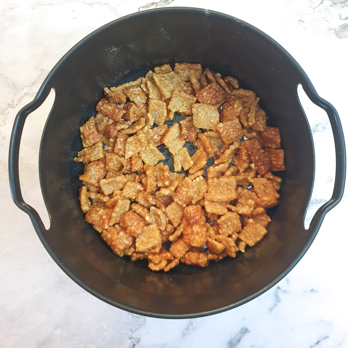 An air fryer basket with cooked pork scratchings.