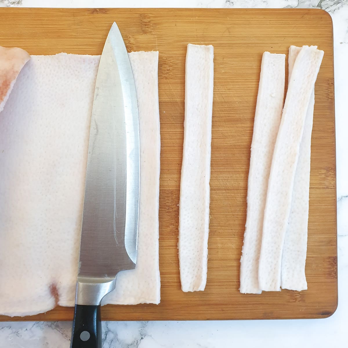 Three strips of pork skin cut from a piece of pork skin.