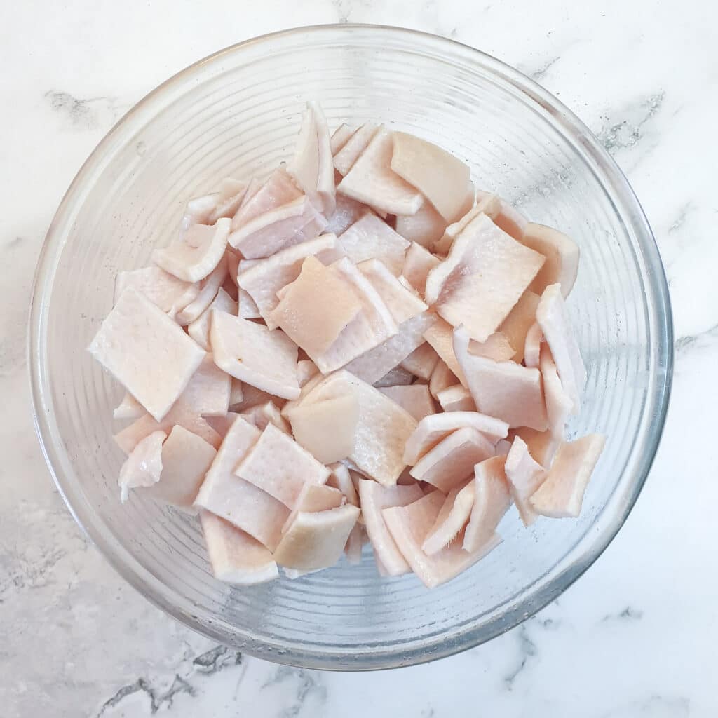 A glass bowl containing pieces of pork skin coated with salt and oil.