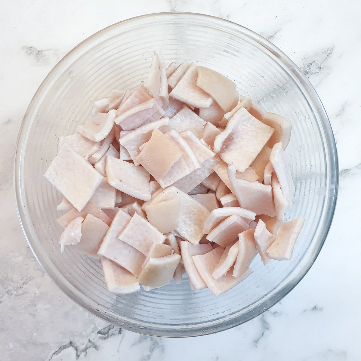 A glass bowl containing pieces of pork skin coated with salt and oil.