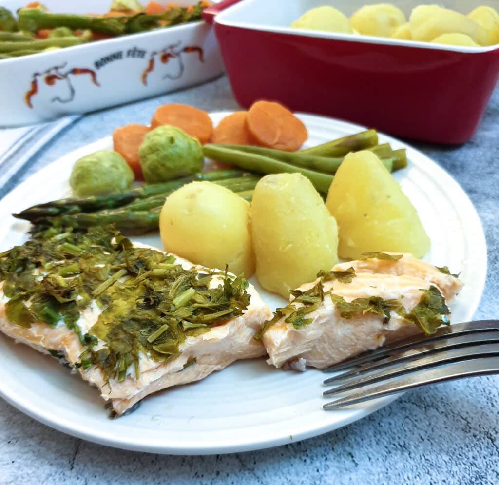 A piece of salmon covered in dill and parsley on a plate with potatoes and vegetables.