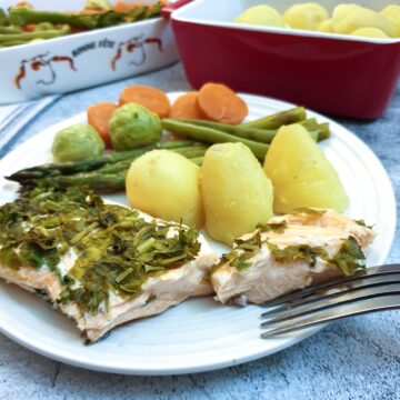 A piece of salmon covered in dill and parsley on a plate with potatoes and vegetables.