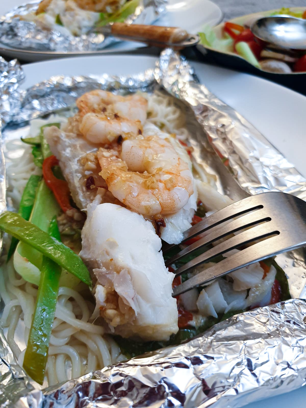 A piece of perfectly cooked fish on a fork held over an opened Thai fish parcel.