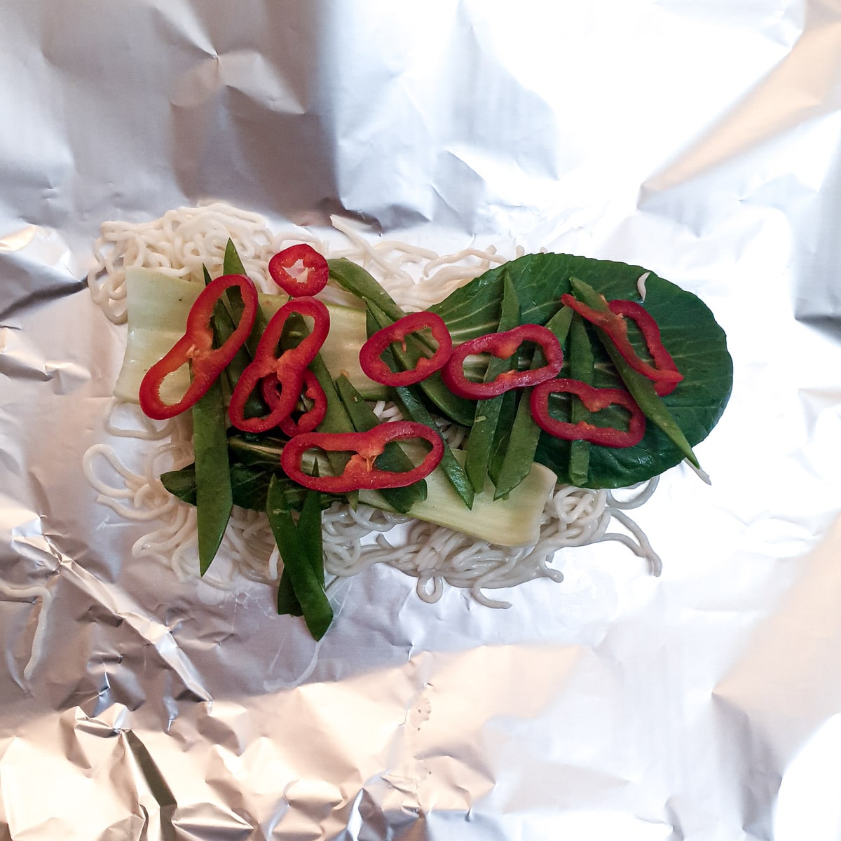 One helping of noodles and vegetables on a sheet of tinfoil.