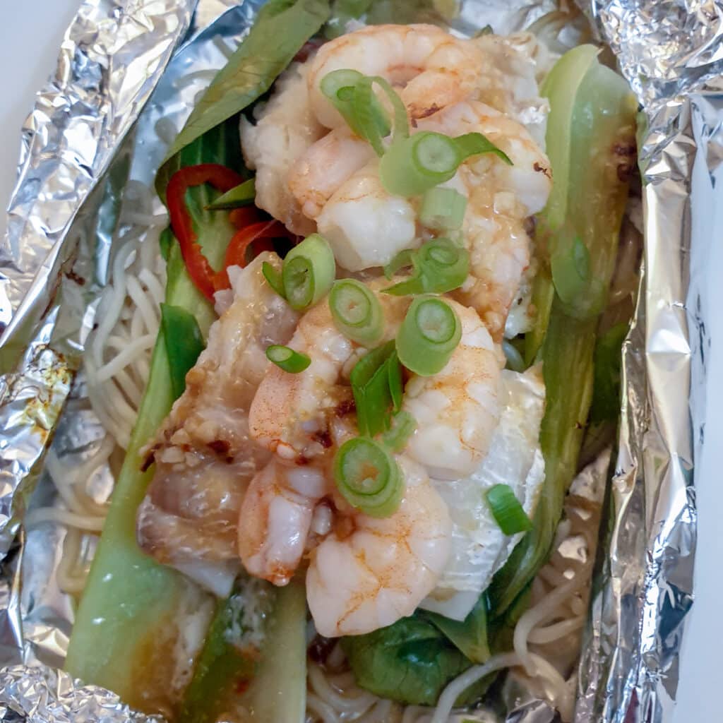 An opened packed to Thai fish and prawns garnished with chopped spring onions