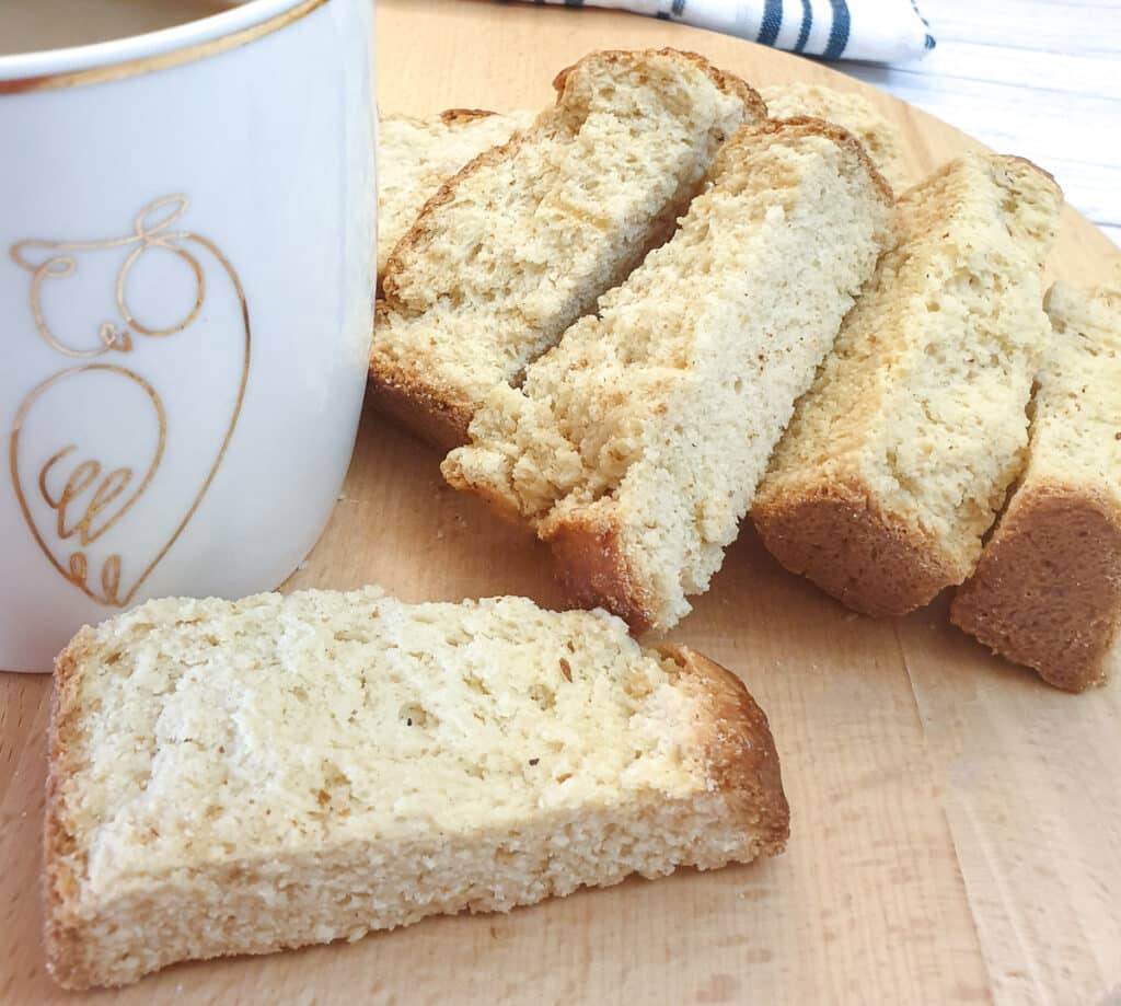 Close up of dried buttermilk rusks on a wooden board next to a cup of coffee.