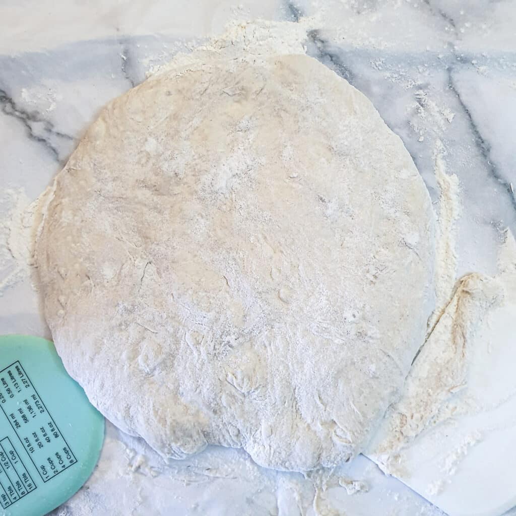 A flattened circle of dough on a floured surface.