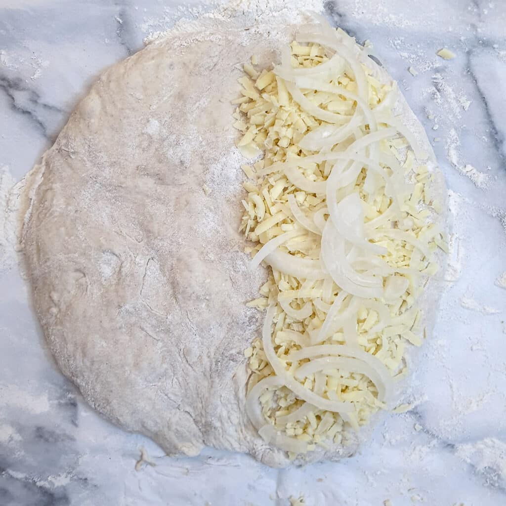 A circle of dough with grated cheese and sliced onions on one half.