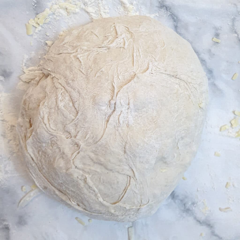 A ball of dough enclosing grated cheese and onions before being placed on a baking sheet.