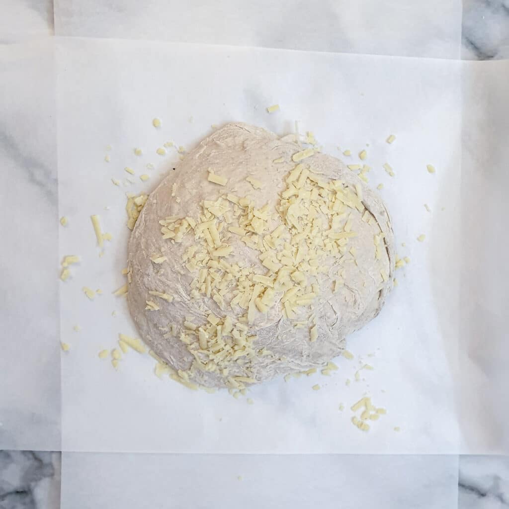 A ball of cheese and onion dough sprinkled with grated cheese.