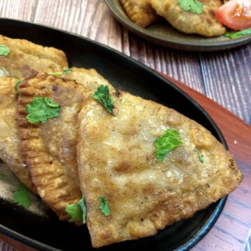 Crispy cheese and sweetcorn samosas on a black plate.