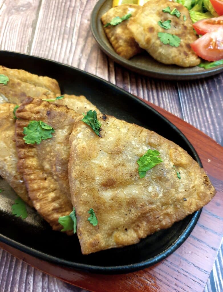 Crispy cheese and sweetcorn samosas on a black plate.