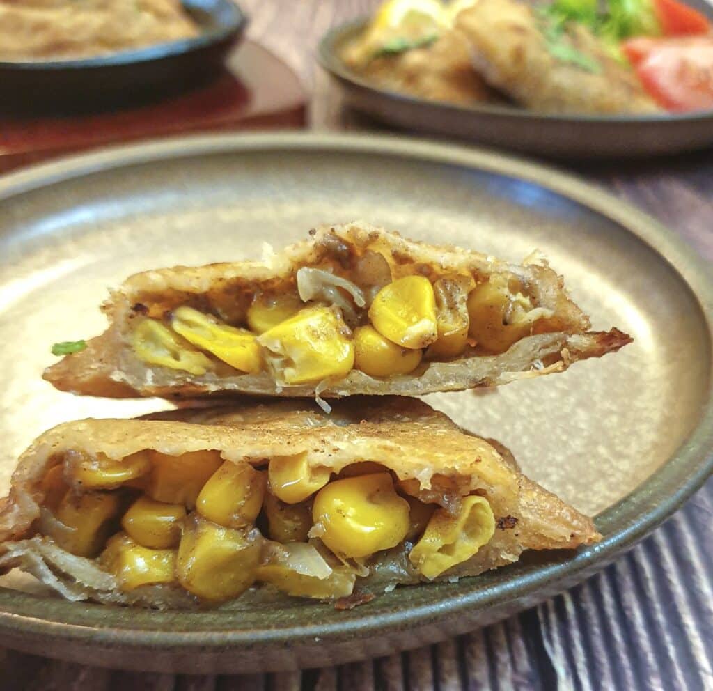 A cheese and sweetcorn samosa cut in half to show the filling.